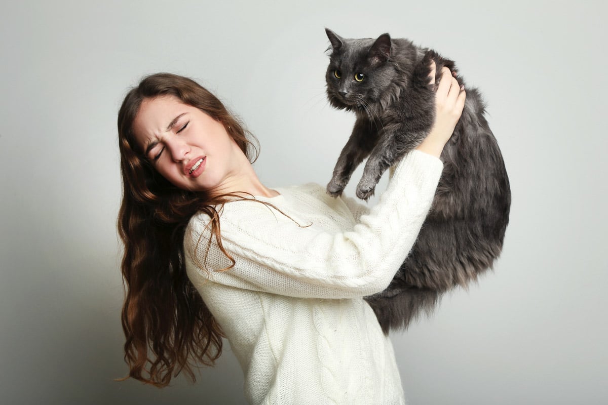 Young woman with allergies hugging a cat on a gray background