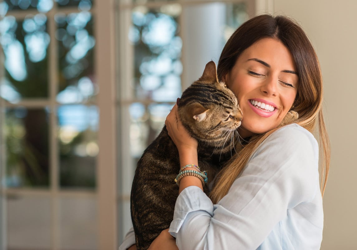Beautiful young woman smiling and lovingly hugging her cat at home