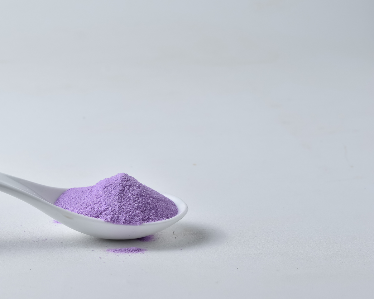 A spoon containing purple taro powder on a simple white background.