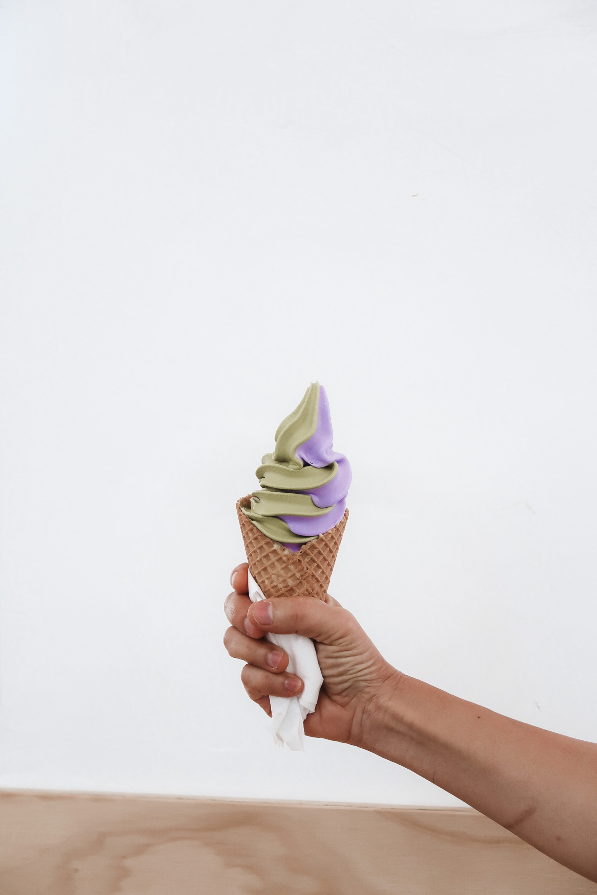 One hand holds out a cone with matcha and taro soft ice cream.