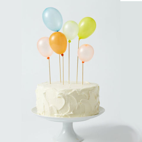 White cake on a white cake stand. Small balloons ordered to make cakes.