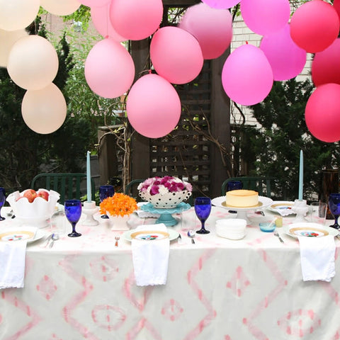 Pink ombre balloons hang on a table frame full of flowers and desserts.