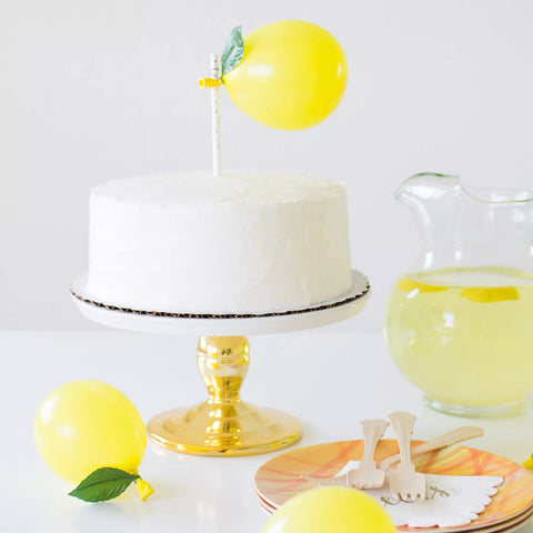 Vanilla cake placed on a cake base plate with a golden base. Small yellow balloons are placed as a cake tray to imitate a lemon.