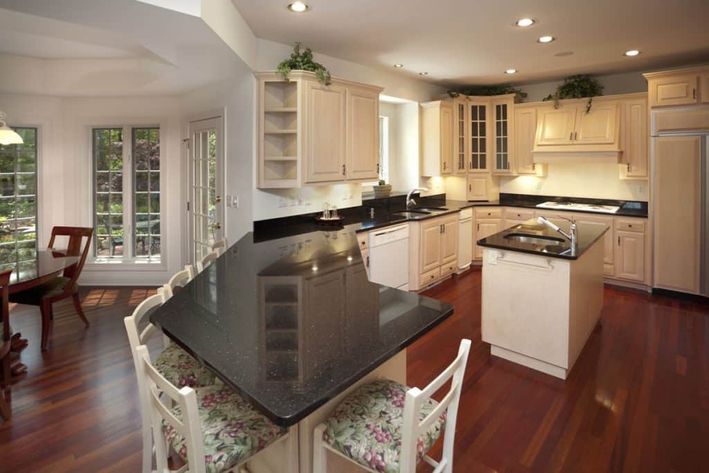 A classic modern kitchen with wood vinyl flooring, black granite countertops and white cabinet panels