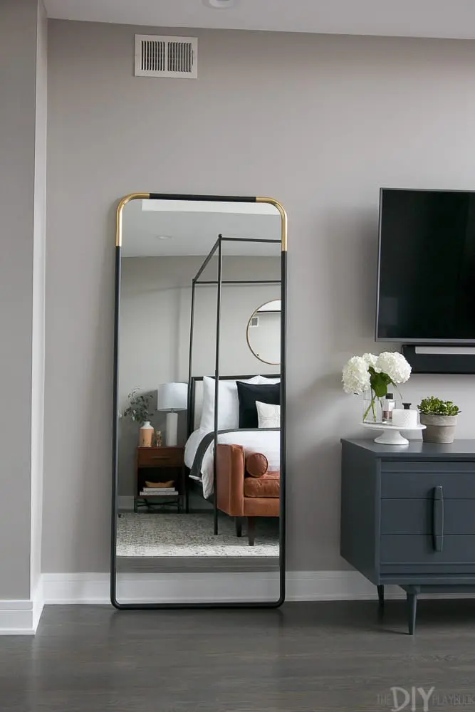 The master bedroom is light and airy with artwork, full length mirror and wooden cupboards.