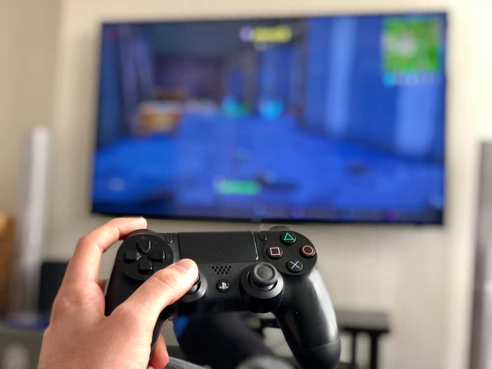 man holds a Sony PlayStation 4 controller while playing a console video game