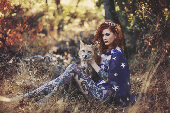 A tattooed female model poses outdoors with a fox