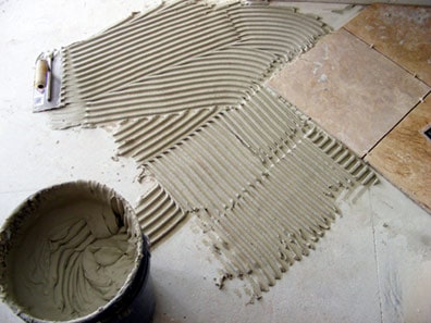 Man's hand brushes a layer of grout, using a notched side.