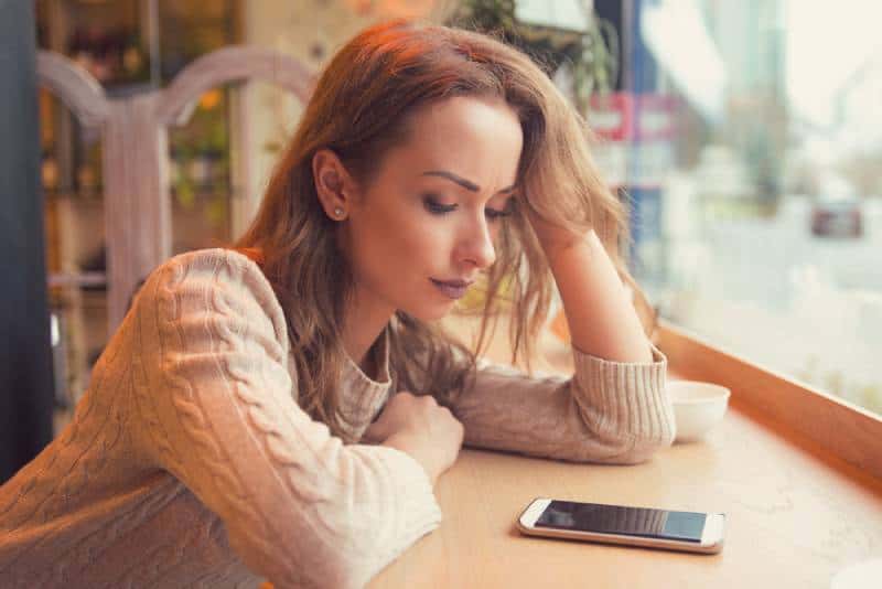 Worried woman looking at her phone at coffee shop