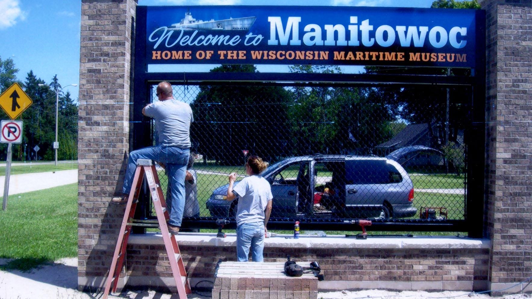 EF Becker and Sons placed the final piece on the “Welcome to Manitowoc” sign on Waldo Avenue. Dean Becker, on the steps, Kim Becker, standing, Tim Becker, behind the sign, and Greg Becker equipping and installing a black chain link panel and emblazoned with the organization's symbols.