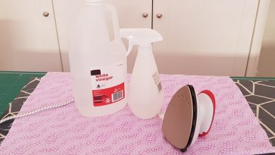 Bottle of white vinegar, spray bottle and iron sitting on creased fabric