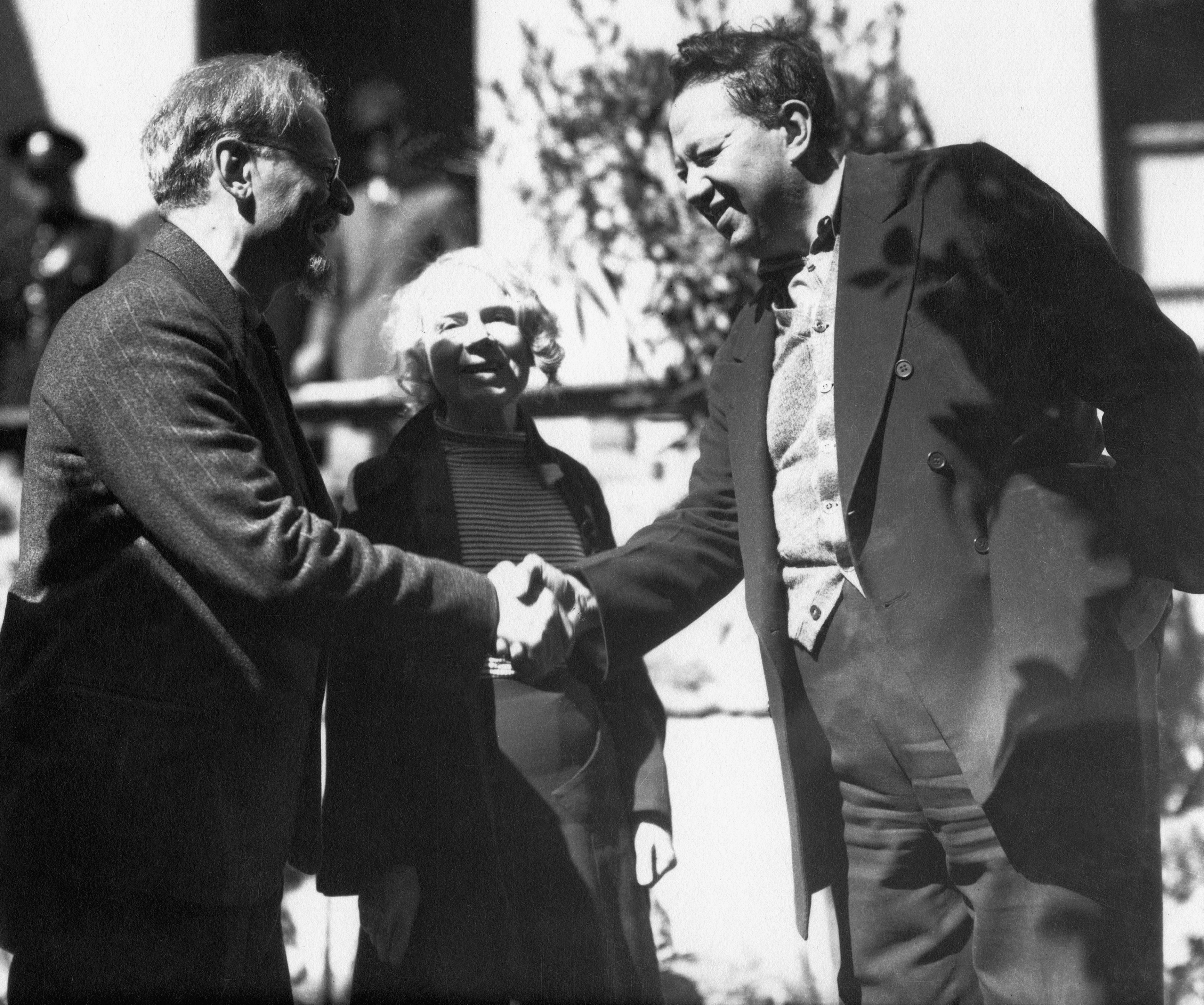 Black and white image of Trotsky and River shaking hands, with a smiling Sedova beside them