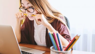 Woman biting a pencil while studying at laptop to avoid failing in college