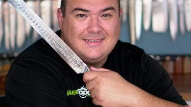 Chef Guga poses in a black tshirt holding a dalstrong carving and slicing knife