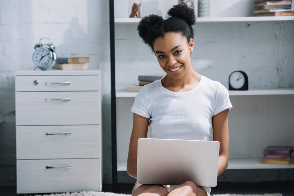 Black girl sitting on floor using laptop with perfect afro puffy hairstyle