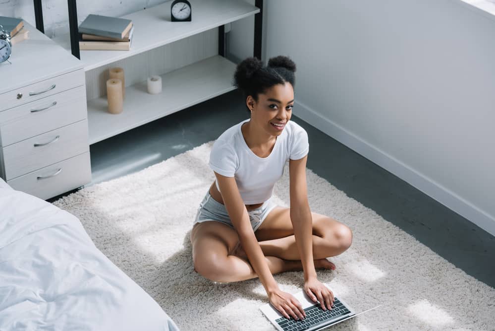 Beautiful black woman using computer on bedroom floor