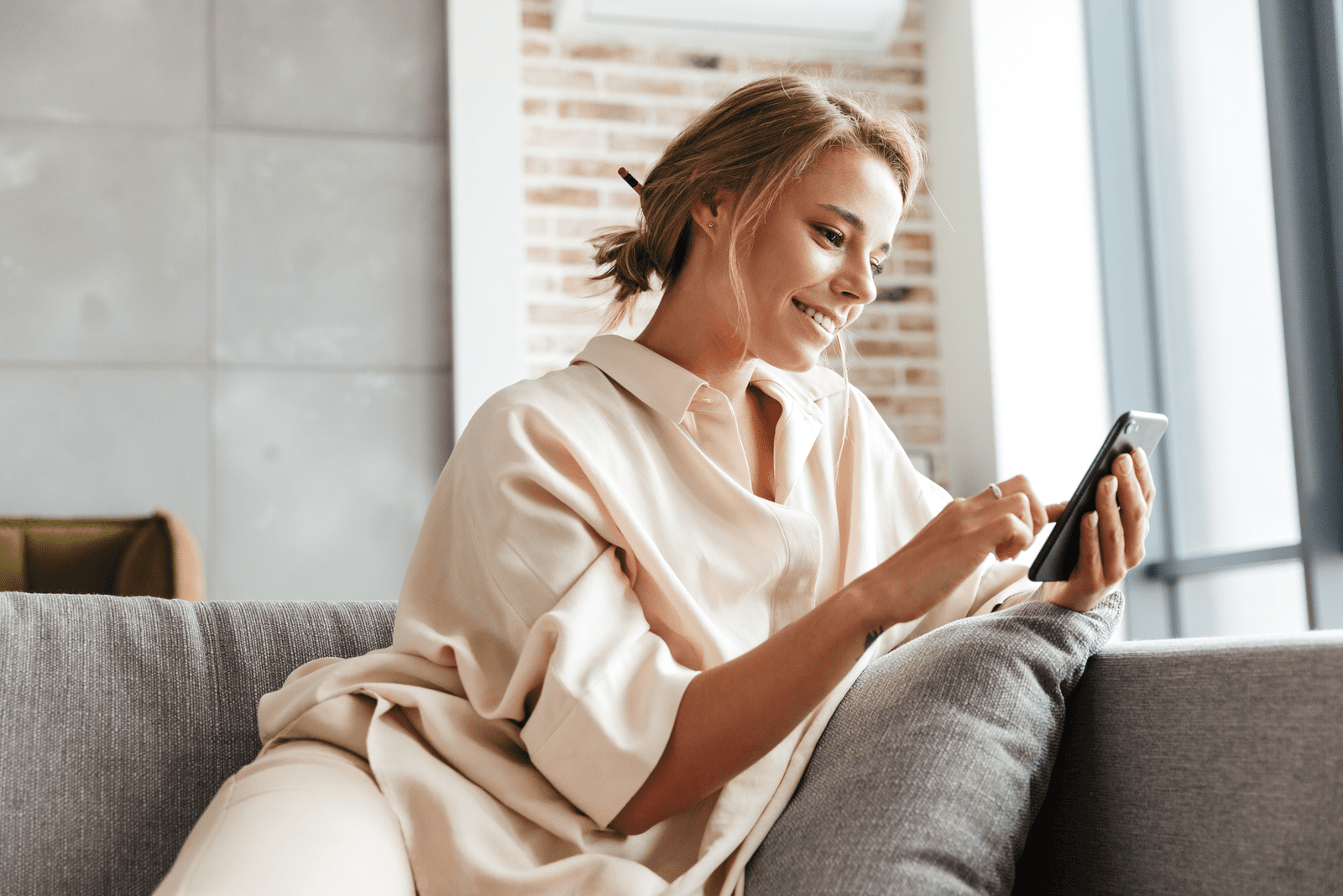 a smiling woman sits on the couch and buttons on the phone