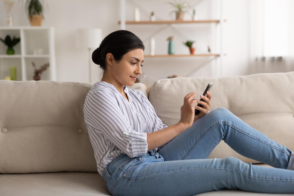 woman spend free time at home sit on cozy sofa at living room texting message in mobile app on smartphone