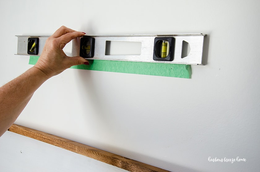 A woman holds a level at the top of a piece of paint tape.