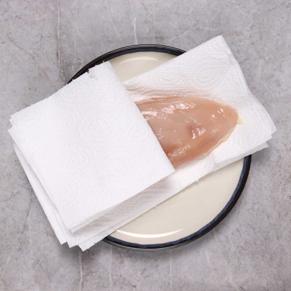 Chicken breast being patted dry before getting seasoning to stick