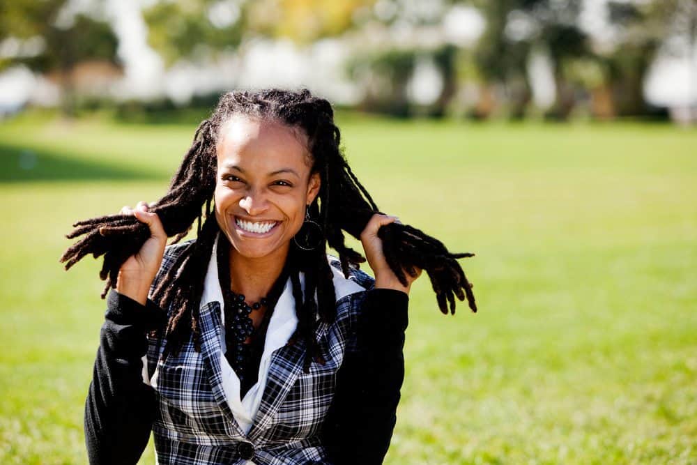 A young African American woman having fun sitting outside holding groups of locs in both hands.
