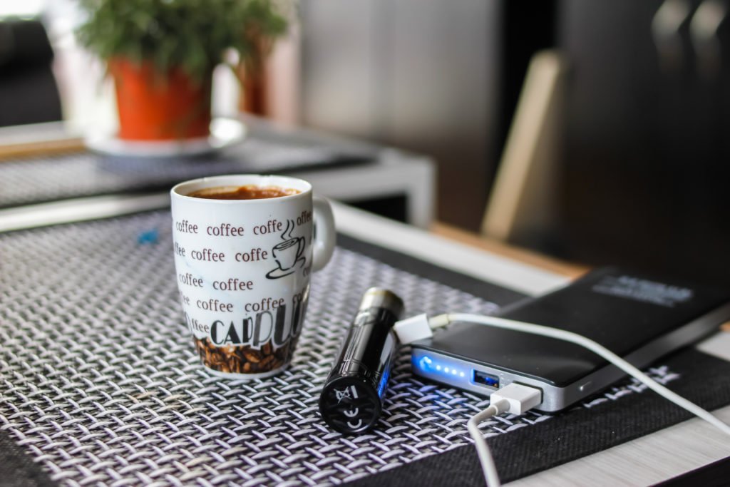 The e-cigarette connects to an electrical outlet next to a cup of coffee.