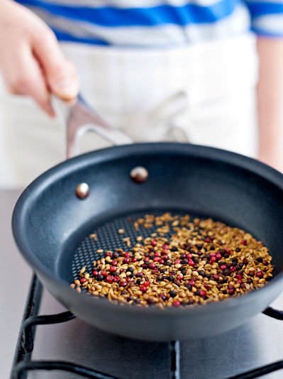 Image of pepper, cumin and coriander seeds being dry roasted on a pan