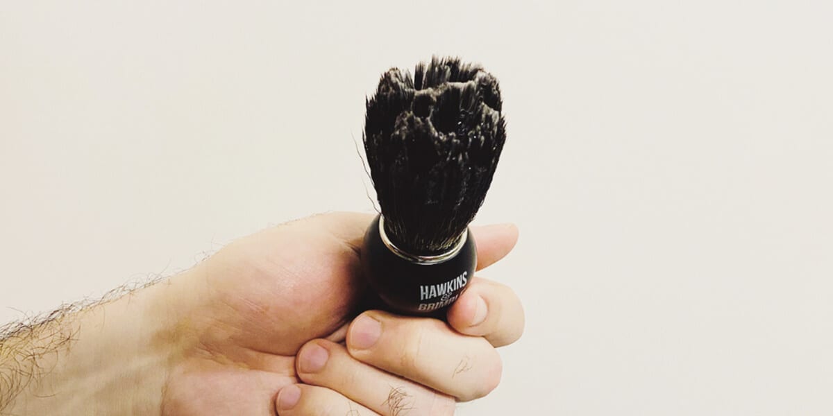 man holding beard brush with shaving cream on it