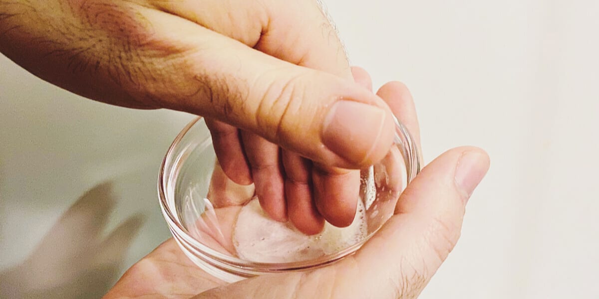 man using fingers to lather shaving cream in a bowl of water