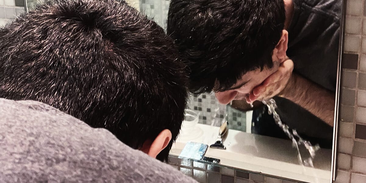 man washing face over bathroom sink, bathroom mirror